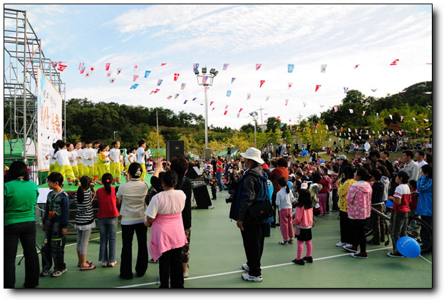 유치원 어린이들이 흥을 돋구고 있고 많은 주민들이 모여 함께 축제를 즐기고 있다.